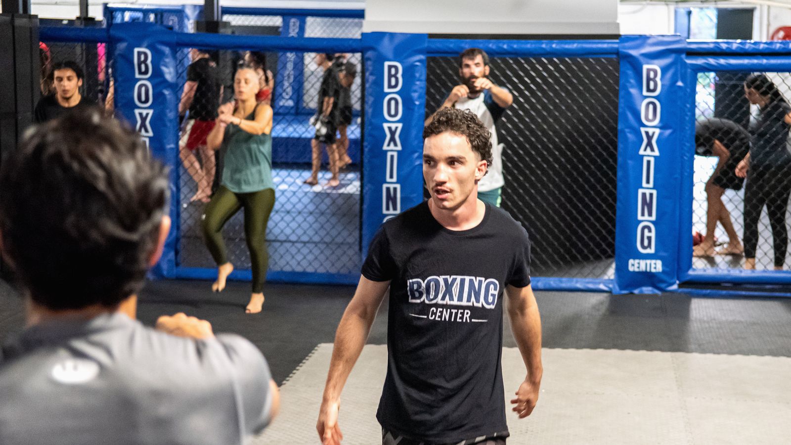 Un adhérent en tee-shirt Boxing Center pendant un cours devant la cage, au club de Toulouse États-Unis