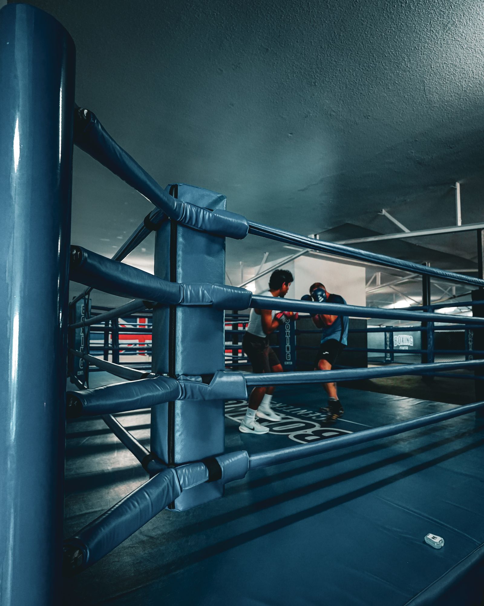 Deux boxeurs en sparring sur le ring du Boxing Center Toulouse États-Unis, vus entre les cordes depuis le coin